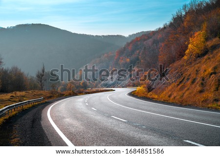 Autumn landscape with road in mountains. Travel background. Highway in mountains under clear blue sky.