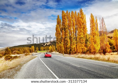Autumn landscape with road and red car, New Zealand