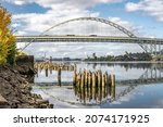 Autumn Landscape with transportation double-story Fremont Bridge with big arched support over the Willamette River in Portland with water reflection and remnants of the piles of the old pier