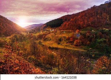 가을 풍경. 언덕 위에 있는 마을. 붉고 노란 잎으로 뒤덮인 산 위의 숲. 산 위로 불빛이 언덕 꼭대기에 있는 개간장에 떨어진다. 스톡 사진