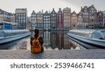 As autumn leaves swirl gently in Amsterdam, a solitary figure enjoys the picturesque view of historic canal houses.