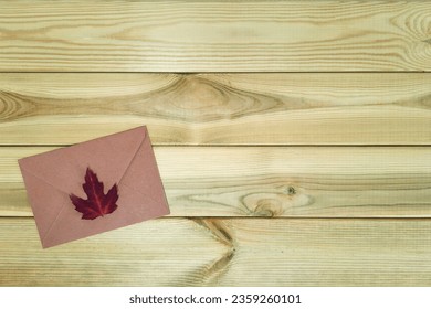 Autumn letter. Copy space. Top view. Brown envelope with a dark red leaf on a wooden table. Autumn seal. Melancholic mood, memories, diary.