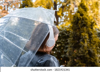 Autumn. Lonely sad woman in a headphones walking in a park, garden. View through wet  transparent umbrella with rain drops. Rainy day landscape. - Shutterstock ID 1821921341