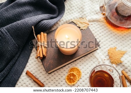 Autumn mood, a burning candle, a book and a kettle of hot tea on a cozy plaid. Atmospheric, romantic mood