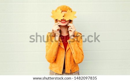 Autumn mood! happy smiling woman holding in her hands yellow maple leaves covering her eyes over gray wall background