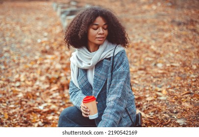 Autumn Mood. Young Happy African American Woman With Curly Hair In Fall Park Holding Take Away Coffee, Looking Aside And Smiling, Relaxing In Nature, Enjoying Her Favorite Season. Selective Focus