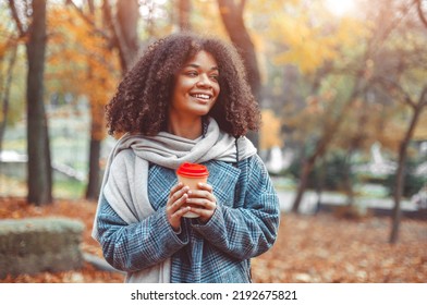 Autumn Mood. Young Happy African American Woman With Curly Hair In Fall Park Holding Take Away Coffee, Looking Aside And Smiling, Relaxing In Nature, Enjoying Her Favorite Season. Selective Focus