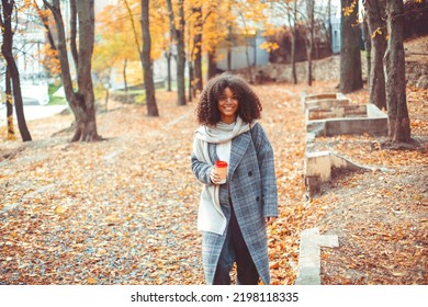 Autumn Mood. Young Happy African American Woman With Curly Hair In Fall Park Holding Take Away Coffee, Looking Aside And Smiling, Relaxing In Nature, Enjoying Her Favorite Season. Selective Focus