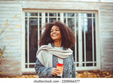 Autumn Mood. Young Happy African American Woman With Curly Hair In Fall Park Holding Take Away Coffee, Looking Aside And Smiling, Relaxing In Nature, Enjoying Her Favorite Season. Selective Focus