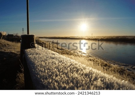Autumn, morning frost on a bench against the background of the river and the rising sun