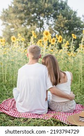 Autumn Nature. Fun And Liesure. Young Teenage Couple Picnic On Sunflower Field In Sunset, Enjoying Time Together, Rear View