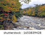 Autumn in New Hampshire. Swift-flowing Pemigewasset River with distant mountain and colorful foliage along river banks.