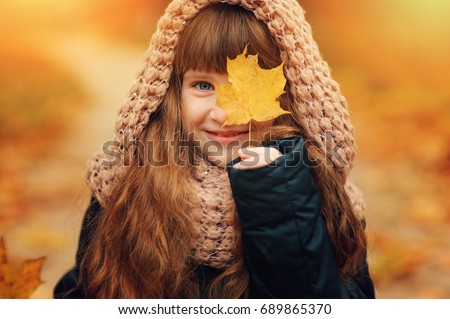 autumn outdoor portrait of beautiful happy child girl walking in park or forest in warm knitted scarf