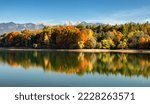 Autumn panoramic landcape with reflection of colorful trees in water and mountains at background. Water reservoir Liptovska Mara and Western Tatras mountains in Slovakia.