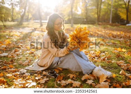 In the autumn park, a happy woman in stylish clothes and a camera is having fun among the fallen leaves. Smiling tourist woman enjoys warm sunny weather in autumn season.