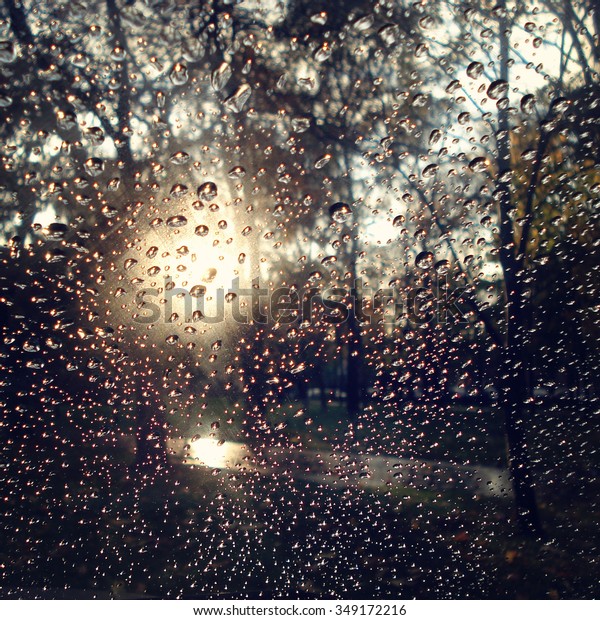 Autumn park through car glass.\
Retro filter. Drops of rain on the car window. Aged photo. Glare\
from the sun through wet window glass. Rainy day in the\
city.