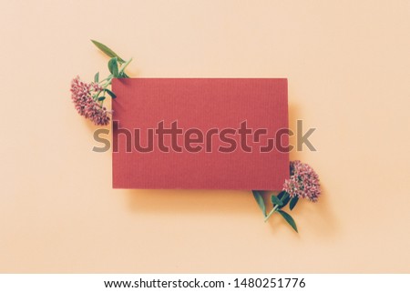 Autumn party invitation. Pale maroon mockup paper sheet with green floral decoration on pastel peach background. Copy space.