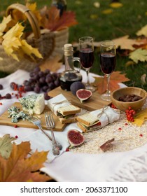 Autumn Picnic With Food, Fruits, Cheese And Red Wine On Lawn With Maple Leaves. Romantic Dinner In Evening Garden