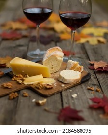 Autumn Picnic With Glasses Of Red Wine, Bread And Cheese On Wooden Table With Maple Leaves. Romantic Dinner In Garden In Evening Outdoors. Still Life