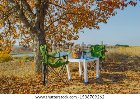 Autumn picnic in the mountains on the lake, a warm autumn day. Basket with food on the table. Herbal tea, thermos on the background of autumn forest and mountains.Autumn concept.