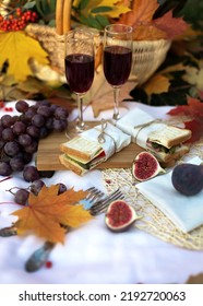 Autumn Picnic With Sandwich, Fruits And Glasses Red Wine In Garden With Maple Leaves. Romantic Dinner In Evening Outdoors. Still Life