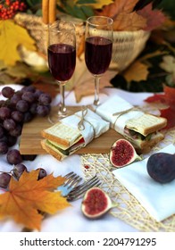 Autumn Picnic With Sandwich, Grapes And Glasses Red Wine In Garden With Maple Leaves. Romantic Dinner In Evening Outdoors. Still Life