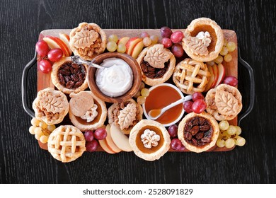 Autumn pie theme dessert board. Above view table scene against a black wood background. Pumpkin, apple and pecan mini pies, with whipped cream, caramel and fruit.  - Powered by Shutterstock