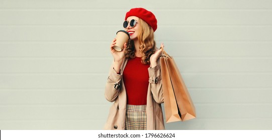 Autumn Portrait Of Attractive Young Woman With Shopping Bag And Coffee Cup Wearing Red French Beret Over Gray Background