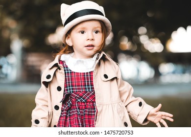 Autumn Portrait Of Baby Girl 2-3 Year Old Wearing Stylish Trench Coat And Hat Outdoors In Park. 