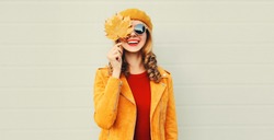 Autumn Portrait Of Beautiful Happy Smiling Young Woman With Yellow Maple Leaves Wearing A French Beret Hat, Sunglasses And Jacket On Gray Background