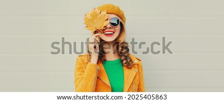 Autumn portrait of beautiful happy smiling young woman with yellow maple leaves wearing a french beret on gray background