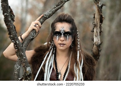 Autumn Portrait Of A Female Viking Wearing Face Paint, Braids, Leather And Fur. She Is Standing In The Forest. 