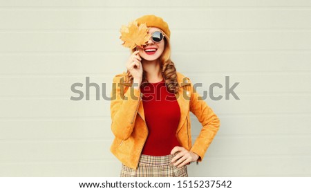 Autumn portrait happy smiling woman holding in her hands yellow maple leaves covering her eye over gray wall background