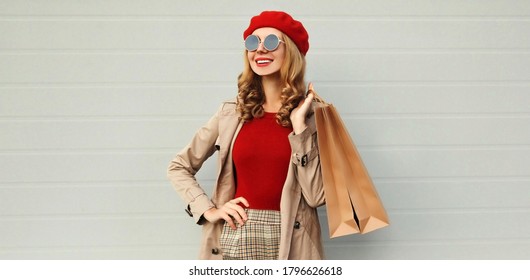 Autumn Portrait Of Smiling Woman With Shopping Bag Looking Away Wearing A Coat, Red French Beret Over Gray Background