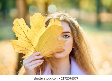 Autumn portrait woman holding in her hand yellow maple leaves covering her eye on fall nature background