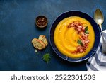 Autumn pumpkin soup with smoked bacon in a blue plate over dark slate, stone or concrete background. Top view with copy space.