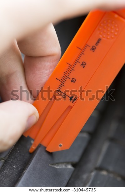 Autumn and the rains are coming. It\'s time to check the\
tyre wear. In this image a person is measuring a tyre wear with a\
specific tool. 