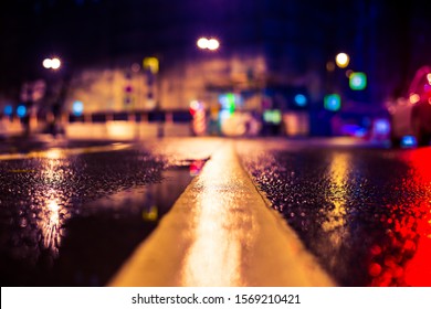 Autumn rainy night in the city. Empty road. Residential buildings in the city center. Colorful colors. Close up view of a puddle on the level of the dividing line.