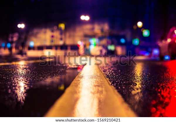 Autumn rainy night in the\
city. Empty road. Residential buildings in the city center.\
Colorful colors. Close up view of a puddle on the level of the\
dividing line.