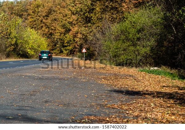 Autumn road in forest with a car. Autumn season\
with sunlight, colorful trees and fallen leaves in the forest.\
Lugoj, Romania, 2019.