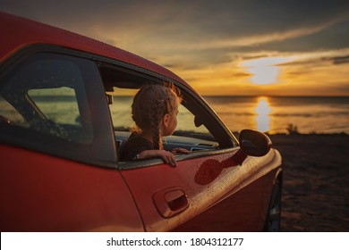 Autumn Road Trip, Freedom And Family Traveler. Pretty Girl Sitting In The Car On The Bank Of Sea, Rest And Leisure, Looking At Beautiful Sunset After Rain, Drops On Windshield, Fall Outdoor Lifestyle