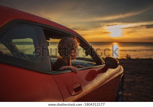Autumn road trip, freedom and family traveler.\
Pretty girl sitting in the car on the bank of sea, rest and\
leisure, looking at beautiful sunset after rain, drops on\
windshield, fall outdoor\
lifestyle