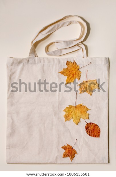 Autumn sale concept. Cardboard labels with percents,\
yellow autumn leaves on eco linen shopping bag over beige\
background. Flat lay.