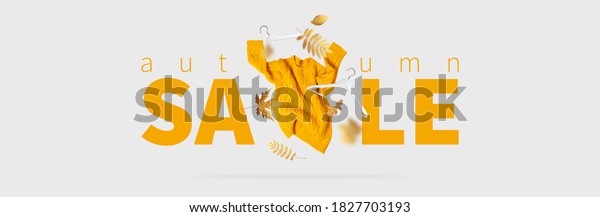 Autumn sale Fall shopping. Orange flying women\'s\
knitted sweater white wooden hangers golden autumn leaves on gray\
background Creative clothing concept trendy fall cozy sweater\
pullover jersey fashion