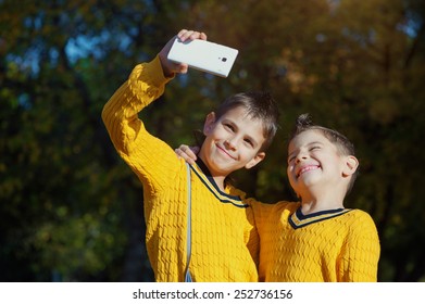 Autumn scene of Happy hugging young brothers taking selfie with a smartphone in the park - Powered by Shutterstock