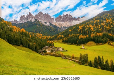 Autumn scenery of Santa Maddalena village and the Church of St. Johann in Ranui, Dolomite Alps, Italy. Lush meadow and autumn-colored trees. Majestic mountain peaks on background
