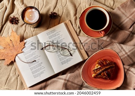 autumn, season and leisure concept - open book of poems with glasses, cup of coffee, cinnamon bun and candle on warm blankets at home