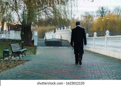 autumn season time morning man in black coat back to camera walking go to work park outdoor paved road along bench and bare trees, loneliness moody depression atmosphere 