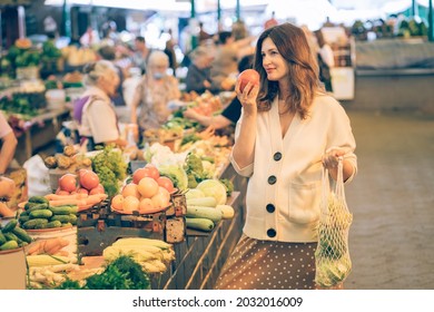 Autumn Shopping At Farmer Market. Good Looking Stylish Pregnant Women Sniff Fresh Tomato During Purchase. Low Waste, Plastic Free Lifestyle Concept. Eco Reusable Shopper Outdoors.