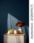 Autumn still life with coffee cup, vibrant pumpkins and flowers on a bedside table against a dark blue wall